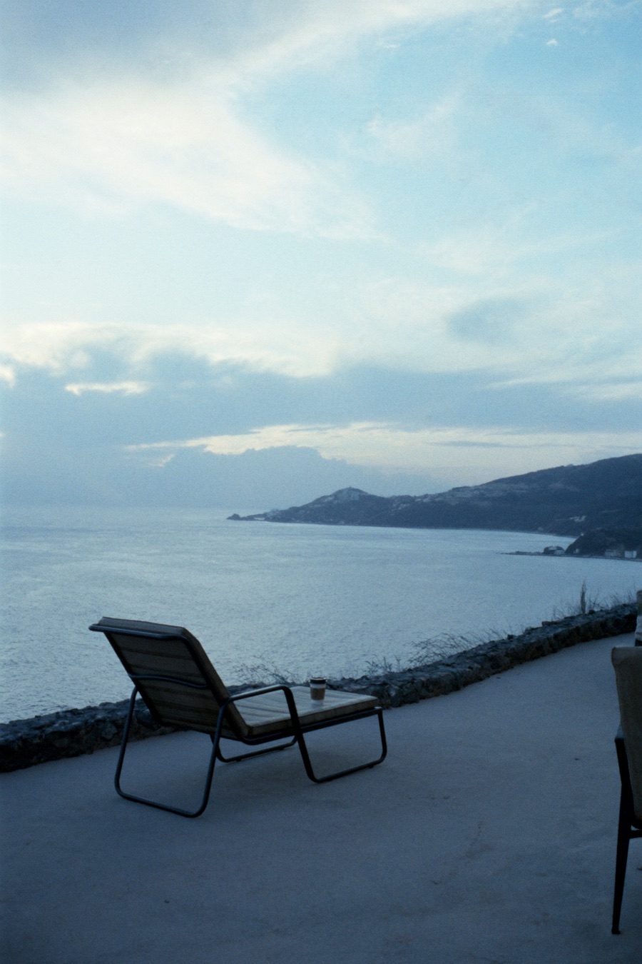 A single lounge chair and coffee on a quiet cliff terrace at dawn