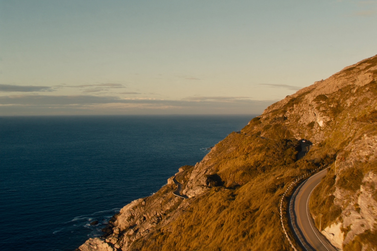 A winding coastal road above a blue sea at golden hour