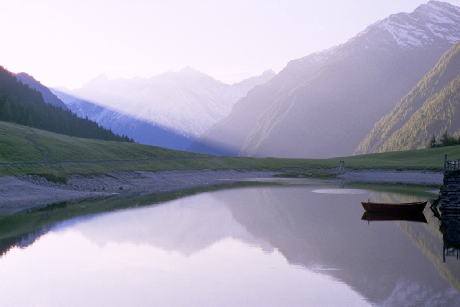 A still alpine lake mirroring misty peaks at dawn
